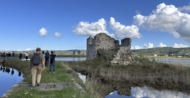 People walking through the Sečovlje Salina Nature Park with blue sky and some clouds and old stone structures